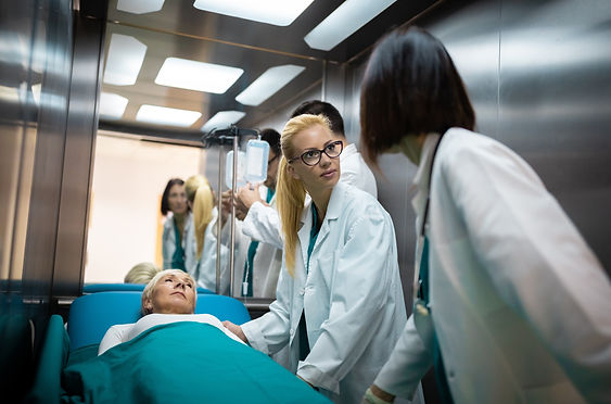 Two female doctors talking in elevator while moving elderly female patient on a gurney wit