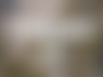 A straight-down aerial view of a small single-engine airplane centered in frame, flying over an airport in bright daylight. The aircraft has a single-piece front windshield and smoothly blended wing roots, with wings and tail clearly visible. Below, intersecting runways, taxiways, ramp areas with hangars, terminal buildings, and parked aircraft form a detailed airport layout, with crisp shadows and high clarity across the scene.