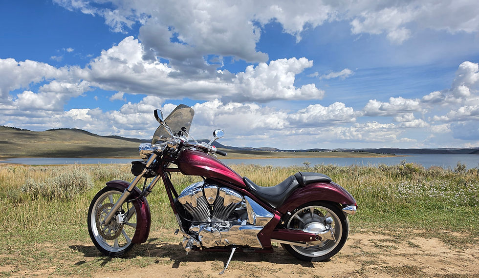 Maroon motorcycle parked on dirt with lake and hills backdrop