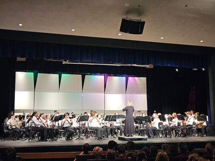 Conductor leads a concert band performing on stage.