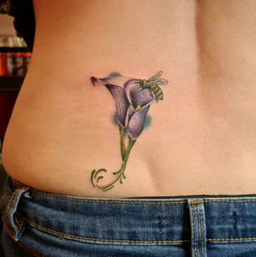 A bee landing on a purple lily tattoo on a ladies back