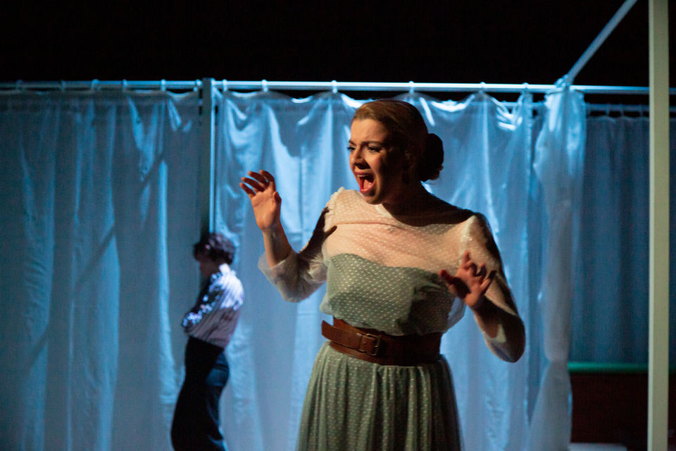 Eine Frau singt oder schreit vor einem hellen Vorhang, im Hintergrund eine andere Person