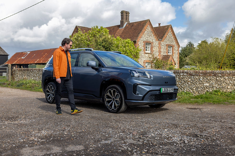 Static front 3/4 shot of a grey AION V with a man walking beside it.