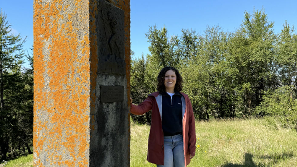 Memorial to Bólu-Hjálmar in Bóla. Maia, a 2024 Snorri participant and Hjalmar's 4xgreat-granddaughter, poses with the Memorial. Photo courtesy of Maia.