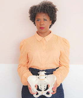 A lady in an orange shirt holding a model of a pelvis