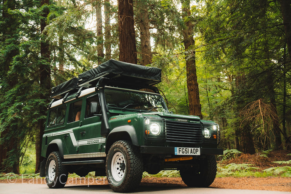 Green Land Rover Defender with roof tent parked on a forest road. Bright headlights, surrounded by tall trees, creating an adventurous mood.