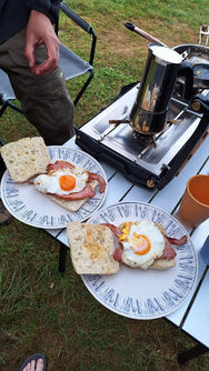 Cooking an english breakfast on a camping stove, with a coffee maker on the stove
