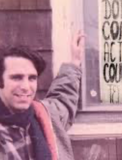 A man smiling while standing next to a sign.