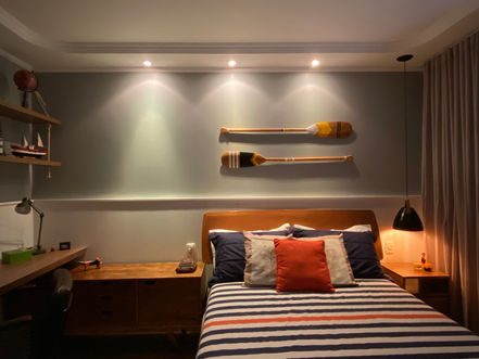 Cama de casal. Cores neutras. Mesa de estudos, prateleiras. Meia parede lambri. Móveis rústicos. Remos decorativos na parede. Iluminação focal.