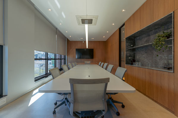 Sala de reuniões terceiro piso. Mesa extensa, com doze cadeiras ao centro. Painel de madeira à direita, com nicho em mármore para café.