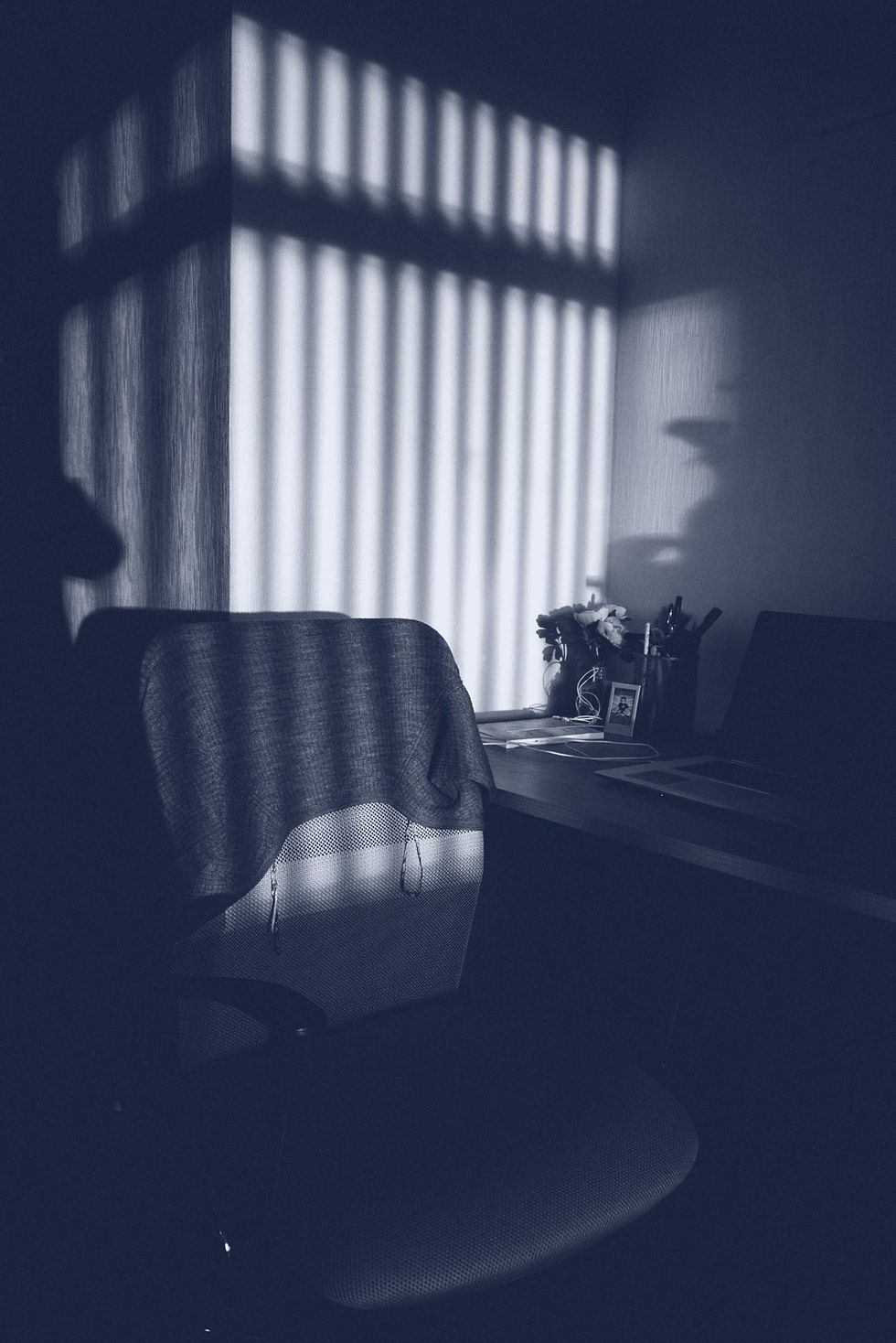 An empty office chair with a sweater over its back, pulled up to a desk in low evening light