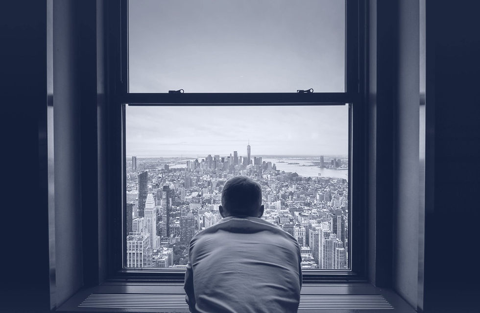 A man seen from behind leaning on a high window ledge, looking out over a city