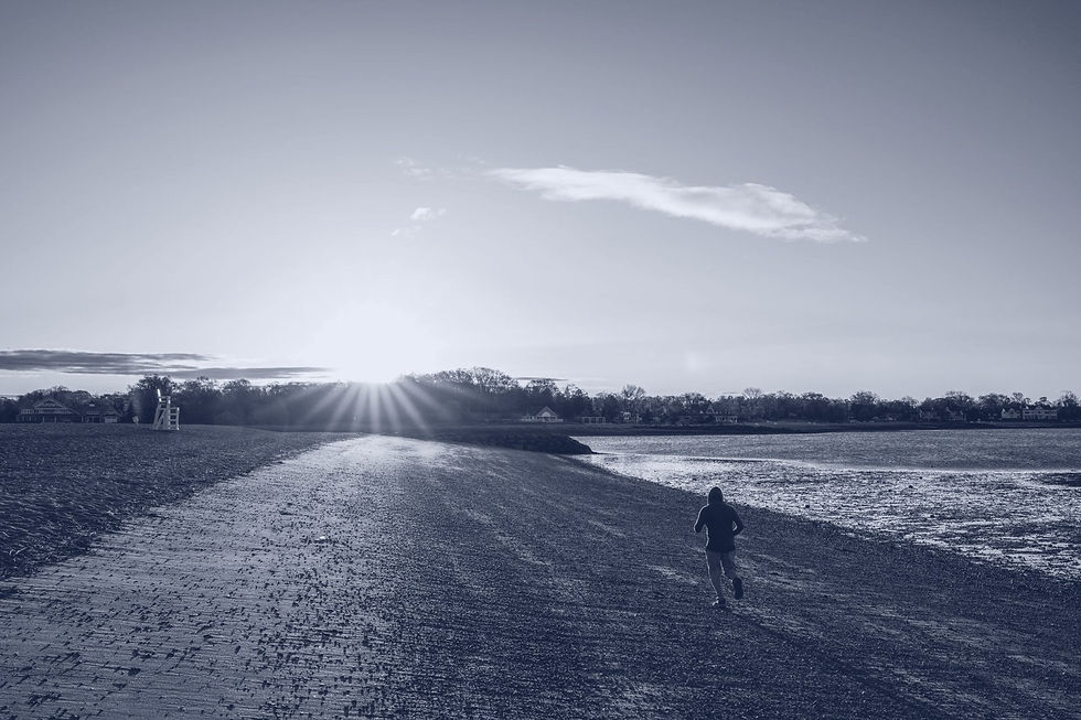 A lone runner seen from behind heading down an empty beach toward the rising sun