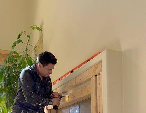 Ari, a drywall and plaster specialist installing plywood to outside of fireplace