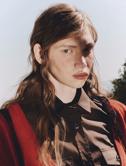 Ritratto beauty di modella con capelli mossi lunghi, camicia nera e cardigan rosso.