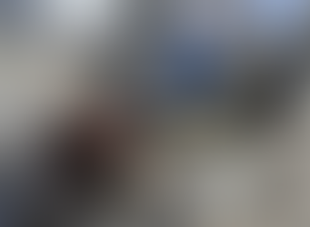 Children stand amid rubble of destroyed buildings, with laundry hanging nearby. Overcast sky and urban surroundings convey a somber mood.