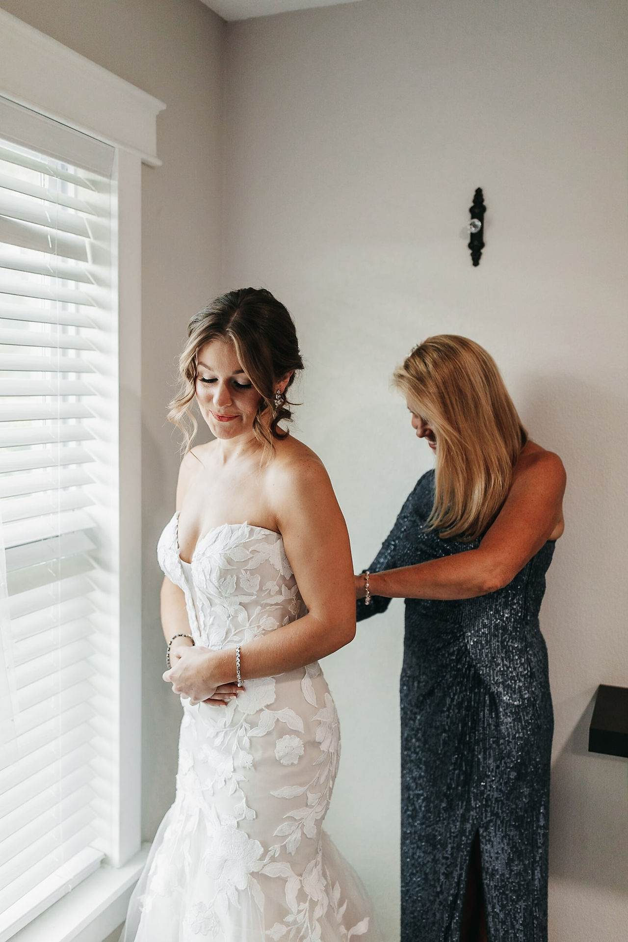 mother of the bride buttoning up bride's dress