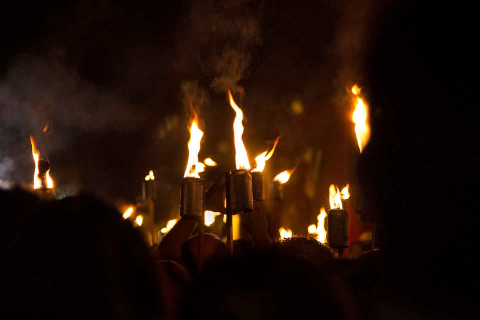 Dezenas de tochas de fogo se aglomeram em um lugar bastante escuro.