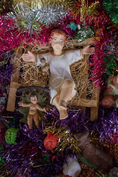 Fotografada de cima, a estátua que representa o menino Jesus no presépio está deitada sobre a manjedoura com os braços abertos.