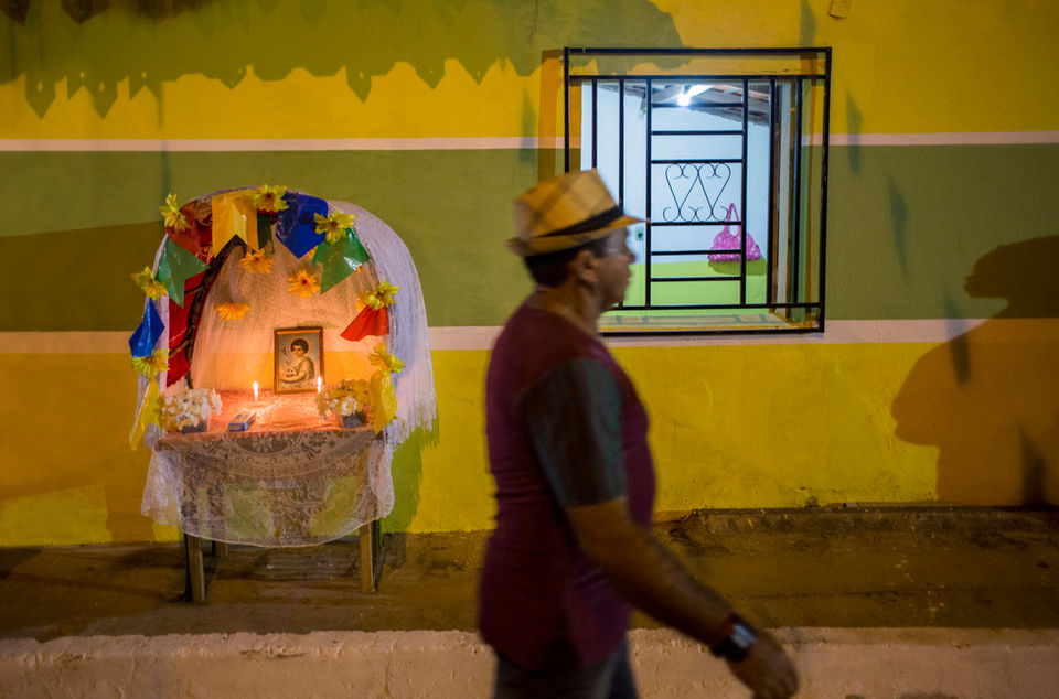 Capelinha de melão com bandeirolas coloridas e a foto de São João numa calçada em Pindaré Mirim. Ao fundo, a parede da casa pintada de verde e amarelo.