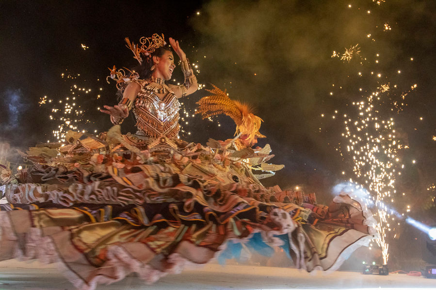 Uma mulher com um vestido rodado, marrom, todo cheio de babados, dança sobre um tablado.