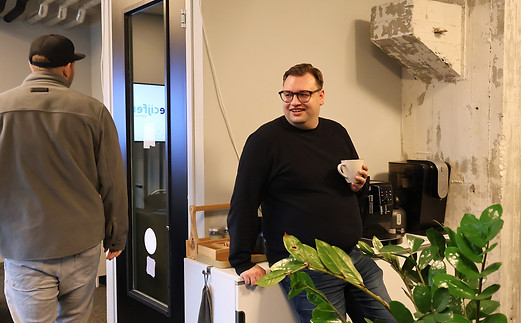 Maurice van vandecijfers staat bij de koffiecorner met een kop koffie en lacht naar een collega in het kantoor in Maastricht