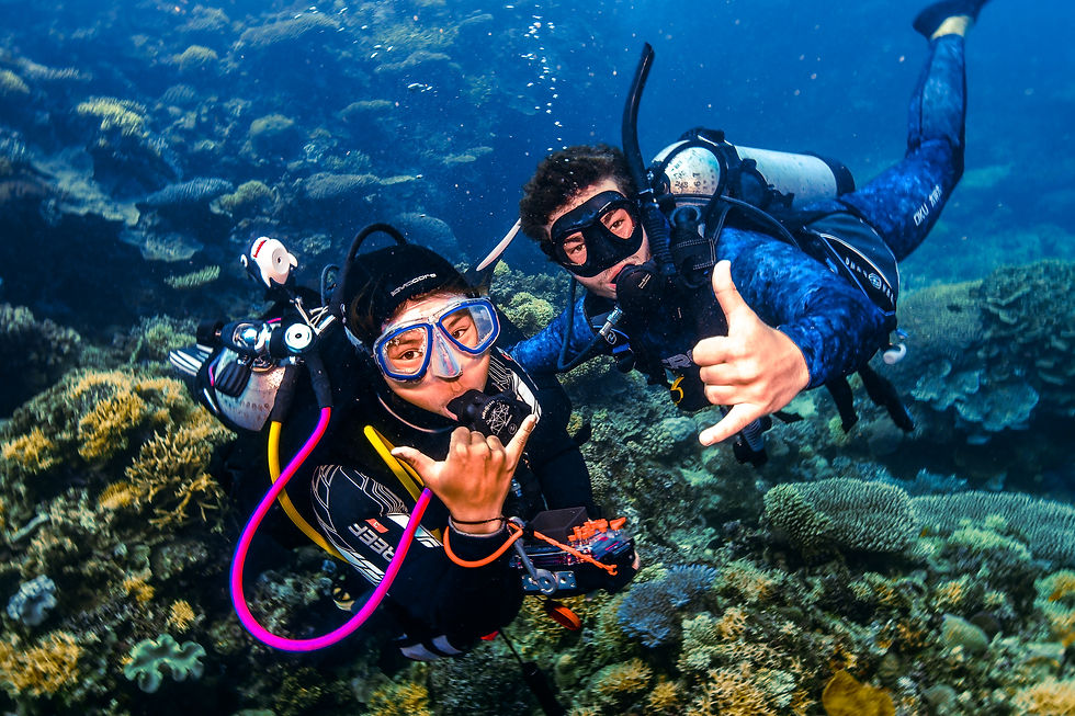 Two scuba divers in vibrant wetsuits make "shaka" signs underwater, surrounded by colorful coral reefs, showing excitement and joy.