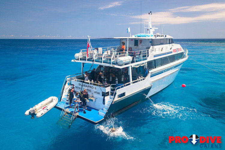 A boat named Scubapro II in clear blue water with divers entering the sea. PRO DIVE is an 3 Day 2 Night Great Barrier Reef Tour from Cairns.
