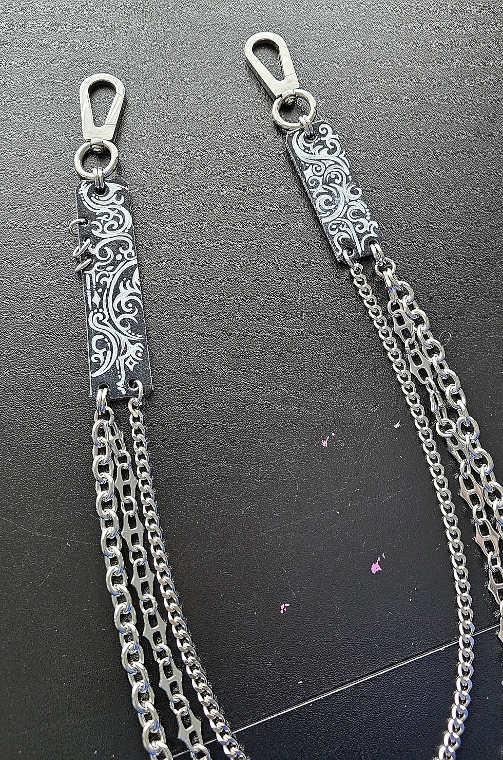Silver chains with ornate metal clips on a black background, featuring intricate white swirling patterns.