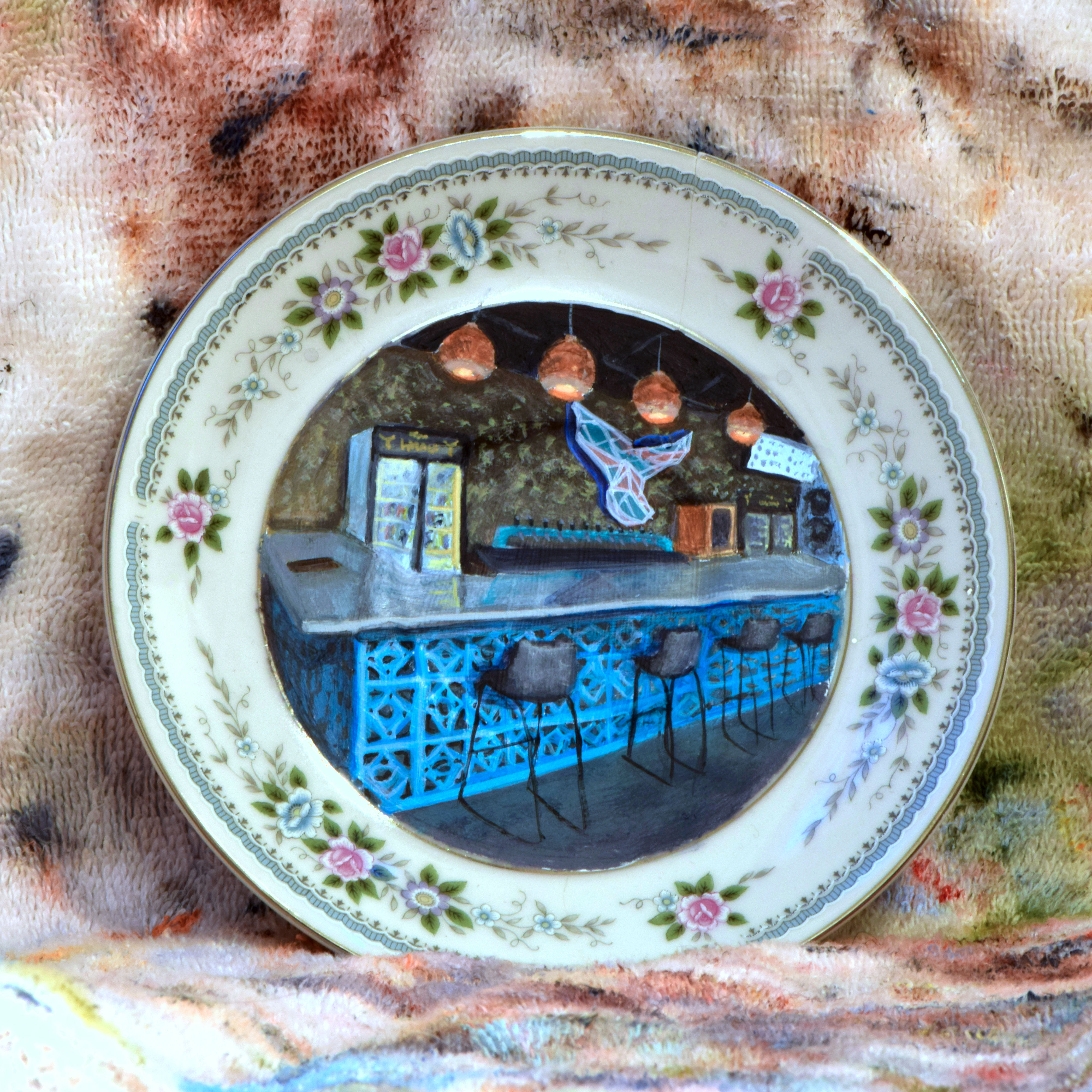 Decorative plate with painted blue bar, stools, and whale tail art.