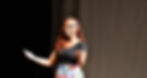 Performer on stage wearing a headset microphone, gesturing expressively during a live performance.