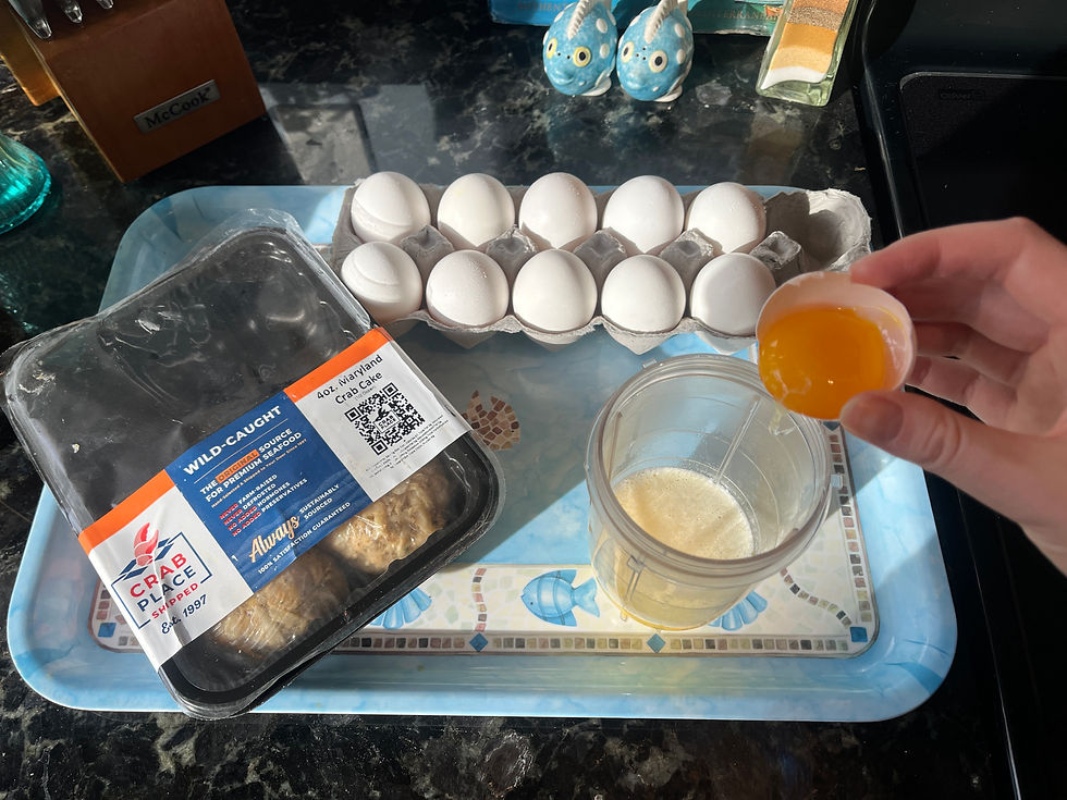 Eggs and Maryland crab cakes on a tray. A hand holds an egg yolk over a blender cup.