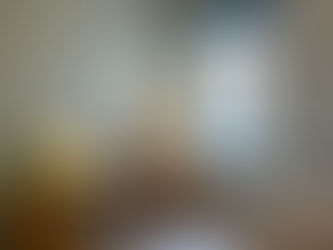 Cosy home office with a wooden desk, laptop, lamp, plant, and chair near a window. Pearl colour walls and a cushion with red patterns on a bench.