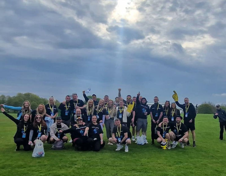 A team of Kilwalk walkers celebrate outdoors as the sun shines down through the clouds.