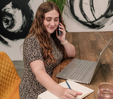Brand photograph of a women working at a table with her laptop and talking on the phone