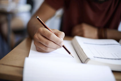 Male student taking notes while reading a textbook