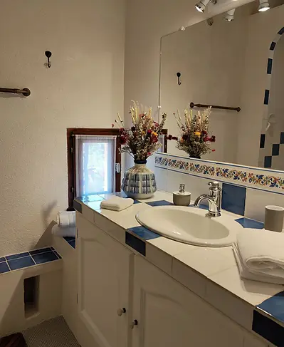 Cuarto de baño de la habitación Canigou con un gran mueble lavabo blanco con azulejos azules, espejo luminoso y ramo de flores secas
