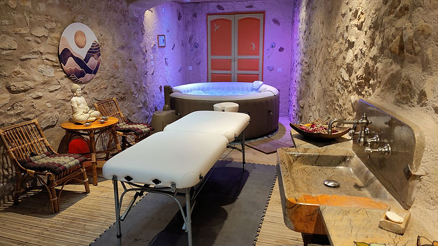 Relaxing spa room featuring a massage table, marble sink, and indoor hot tub surrounded by traditional stone walls at the Mas