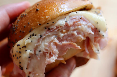 A person holding a ham and cheese sliders with poppyseeds