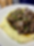 A plate of mashed potatoes with garlic butter steak bites on top. Garnished with chives.