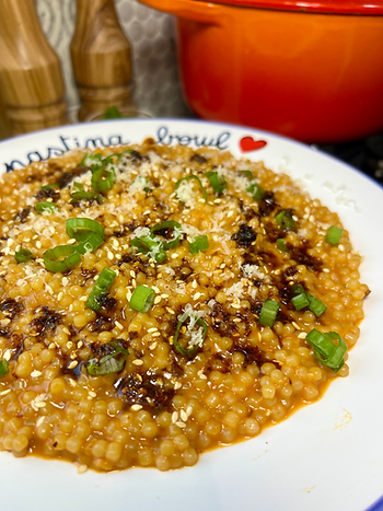 A bowl of creamy pastina garnishd with sesame seeds, scallions, chili oil, and parmesan. Cozy vibes.
