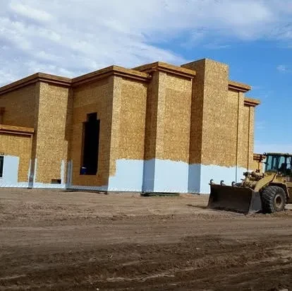 Front loader beside sheathed building exterior during construction