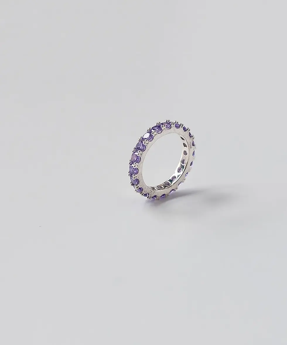 Miniatura: Anel aparador tipo eternity band, inteiramente cravejado com pedras redondas na cor lavanda e metal prateado, posicionado em