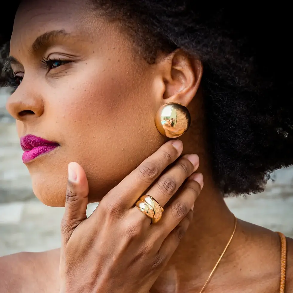 O brinco possui formato circular e volumoso com acabamento espelhado, complementando um look editorial com maquiagem marcante