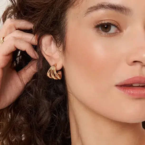 Miniatura: Argola Tripla Orgânica Lèontinte na orelha. O brinco dourado destaca-se pelas linhas fluidas que emolduram o lóbulo com um br