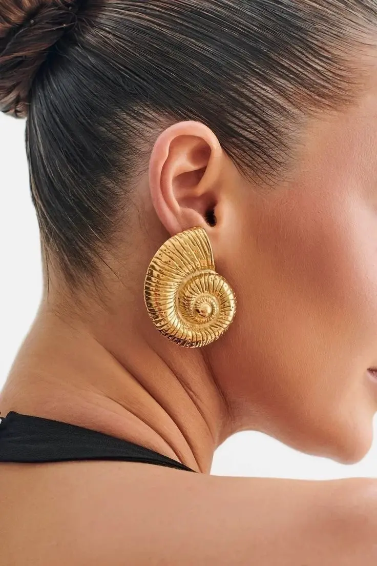 Detalhe de perfil de modelo usando o Brinco Maxi Botão Concha, evidenciando o tamanho e a estrutura da peça na orelha.
