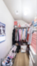Small organized walk-in closet with hanging clothes and shoes
