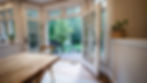 Open French doors leading to a wooden deck and lush garden