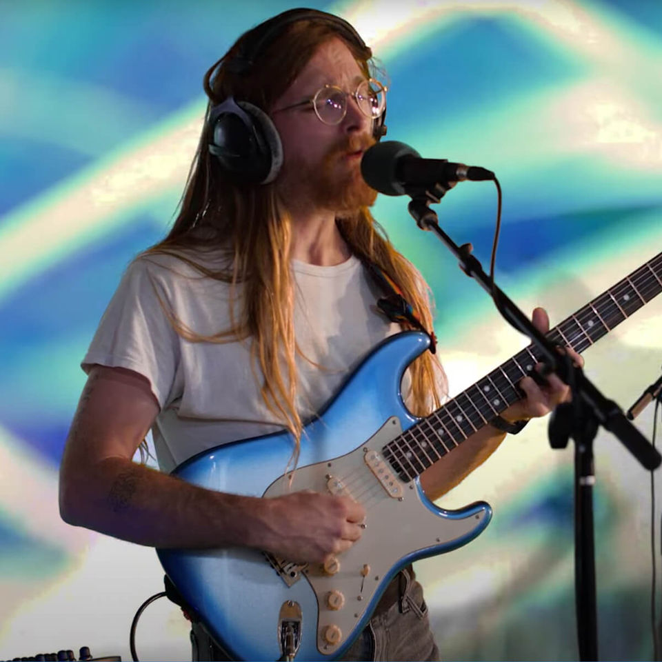 tonstartssbandht guitarist in front of blue and green visuals that are programmed onto a green screen during a live performance in studio.