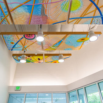 acoustic panels hanging from the ceiling in the lobby feature a colorful painted mural on the surface.